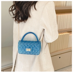 Blue jelly bag with quilted pattern, beaded handle and golden chain strap shown in lifestyle
