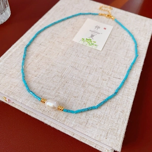 Detail view of turquoise beads and baroque pearl necklace on a textured book surface