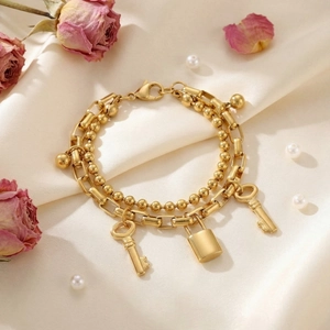 Detail of double-layered gold bracelet with bead chain, key and padlock charms