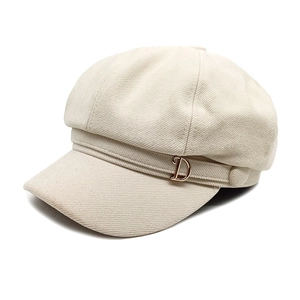 Detail of beige newsboy hat showing twill fabric texture and golden D letter charm