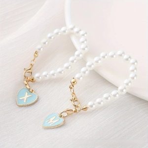 Detail of pearl chain accessory featuring blue heart pendants with gold letters X and M