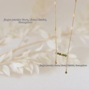 Detail of gold necklace featuring olive green faceted beads and elegant fringe tassels