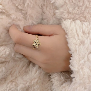 Detailed view of an adjustable golden flower ring on a hand with soft cream background