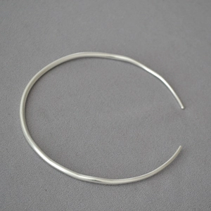 Detailed view of a silver minimalist open collar necklace on a grey fabric background