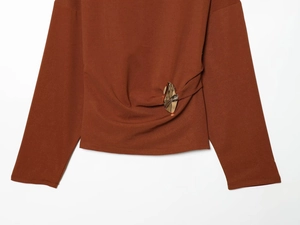 Detail of the golden metal buckle on the dark brown long sleeve top with waist ruching
