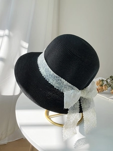 Detail of black woven straw hat featuring a delicate white lace ribbon and bow decoration