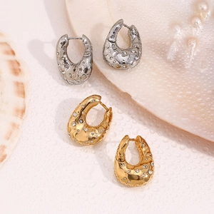 Detailed shot of gold and silver irregular twisted earrings with crystals on a shell