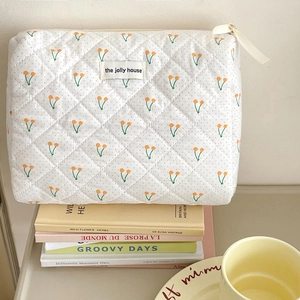 Trousse de maquillage matelassée aux motifs cerises posée sur des livres et café