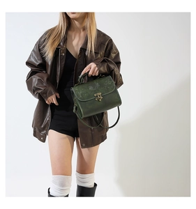 Detail of dark green leather handbag featuring floral embossing and bronze metal clasp