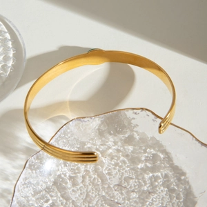 Close-up of golden stainless steel cuff bracelet with green agate stone on glass plate