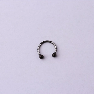 Détail macro du piercing noir en forme de C avec zirconiums sur fond violet doux