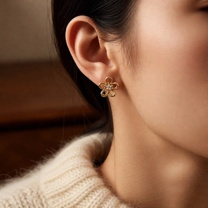 Close-up of golden hollow flower earring with zircon inlay worn by a female model