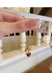 Close-up of a deep red heart pendant necklace with colorful enamel charms on a gold chain