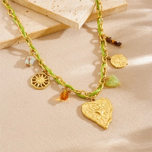 Handmade gold chain necklace with green cord, heart and sun charms on stone background