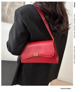 Detail of red leather shoulder bag with gold rectangular metal clasp and smooth finish