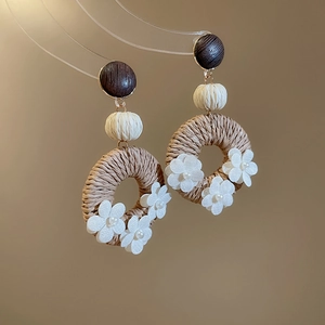 Detail of bohemian handmade woven rattan hoop earrings with white fabric floral accents