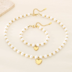 Elegant pearl necklace and bracelet set with golden heart charms on beige surface