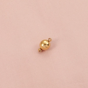 Close-up of a 8mm golden spherical magnetic clasp on pink textured fabric background
