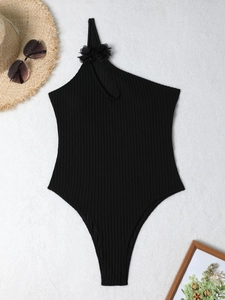 One-shoulder black one-piece swimsuit with floral applique and ribbed texture on beach mat
