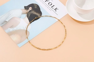 Collier à maillons dorés à plat avec magazine et tasse blanche sur fond pêche