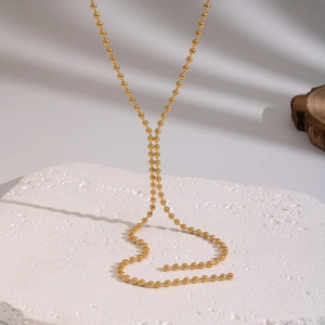 Minimalist gold beaded necklace displayed on a white porous stone with natural lighting