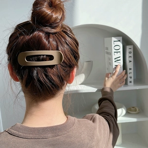 Matte brown oval cutout hair clip styled on a high bun in a modern minimalist room