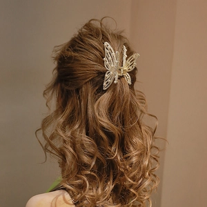 Elegant gold butterfly hair claw clip with pearls worn on wavy brown hair for women