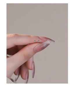 Close-up of green zircon silver stud earrings held by hand for size reference