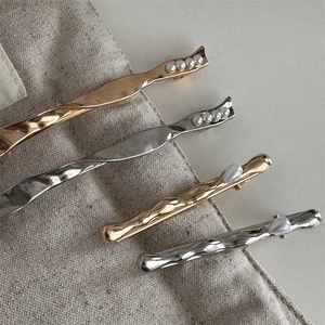 Set of four textured gold and silver hair clips with elegant pearls on linen fabric