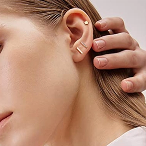 Detail view of gold star, bar, and crystal stud earring set on a model's ear