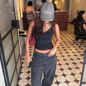 Détail d'un caraco noir avec bordure en dentelle porté avec une casquette grise stylée