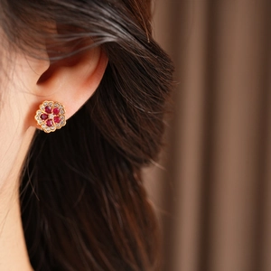 Detail view of flower stud earring with red gemstones and zircons on ear lobe