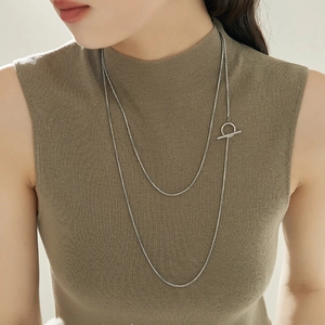 Long silver snake chain necklace with T-bar clasp worn in double-layer style over a sweater