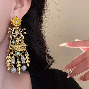 Vintage gold earrings with bird motifs, resin pearls and colorful gemstones on a model
