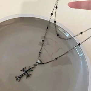 Dark gothic double-layered cross necklace with black stones on a grey ceramic vase