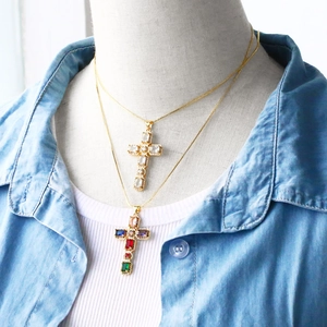 Detail view of cross necklaces with colorful cubic zirconia on a model wearing denim