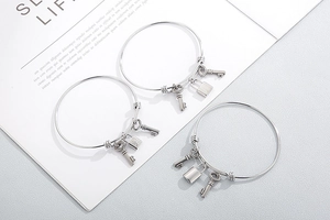 Detailed view of silver stainless steel bangle set with hanging lock and key charms