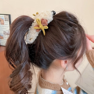 Detail showing plush teddy bear hair clip with bow on model in a cozy home setting