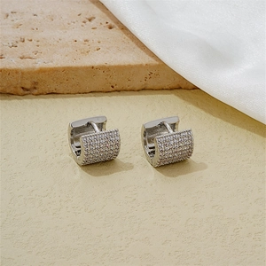 Detailed close-up of silver hoop earrings with cubic zirconia on a textured background
