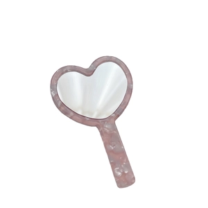 Pink heart-shaped handheld mirror with elegant acetate marble texture on white background