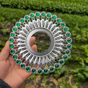 Macro view of a silver metal wall decor disc with radiant patterns and green gemstones