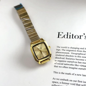 Detail view of square gold watch with metal strap placed on a magazine background