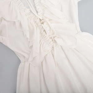 Detail of white V-neck chiffon dress showing layered ruffles and lace-up neckline