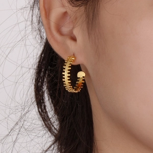 Close-up of golden C-shaped fishbone textured earrings worn by a model in natural light
