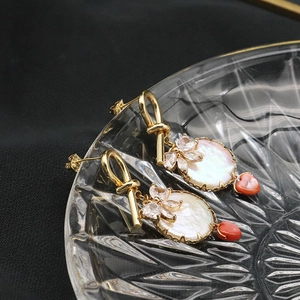 Detail of 18k gold earrings featuring mother of pearl, zircon flower and red heart pendant