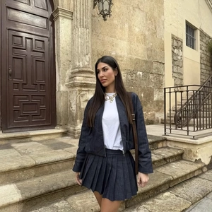 Completo gonna a pieghe in denim blu scuro e giacca coordinata su una scala in pietra