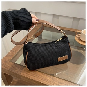 Detail of black textured fabric underarm bag with brown leather strap and gold hardware