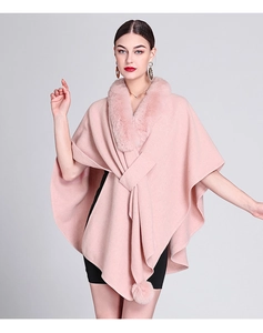 Pink knit cape featuring a plush faux fur collar and decorative hanging pom-poms