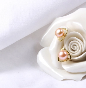 Detailed shot of pink freshwater pearls set in gold triangle studs on white ceramic