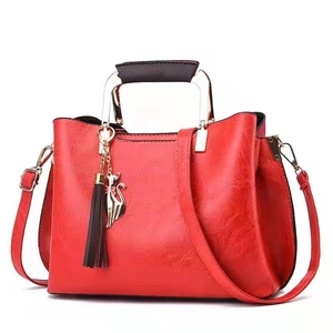 Red crossbody handbag with lychee pattern leather, cat charm and tassel on white background